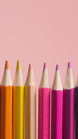 Vertical-Video-Studio-Shot-Of-Multi-Coloured-Pencils-In-A-Line-On-Pink-Background-